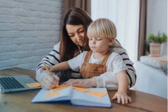Kind mit Wachstumshormonmangel mit Bezugsperson am Tisch, Notizbuch mit Haftnotizen – GHD Patientenperspektive und Alltagsorganisation