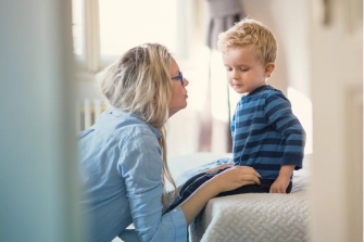 Eine Frau spricht auf Augenhöhe mit einem kleinen Jungen, der auf einem Bett sitzt.